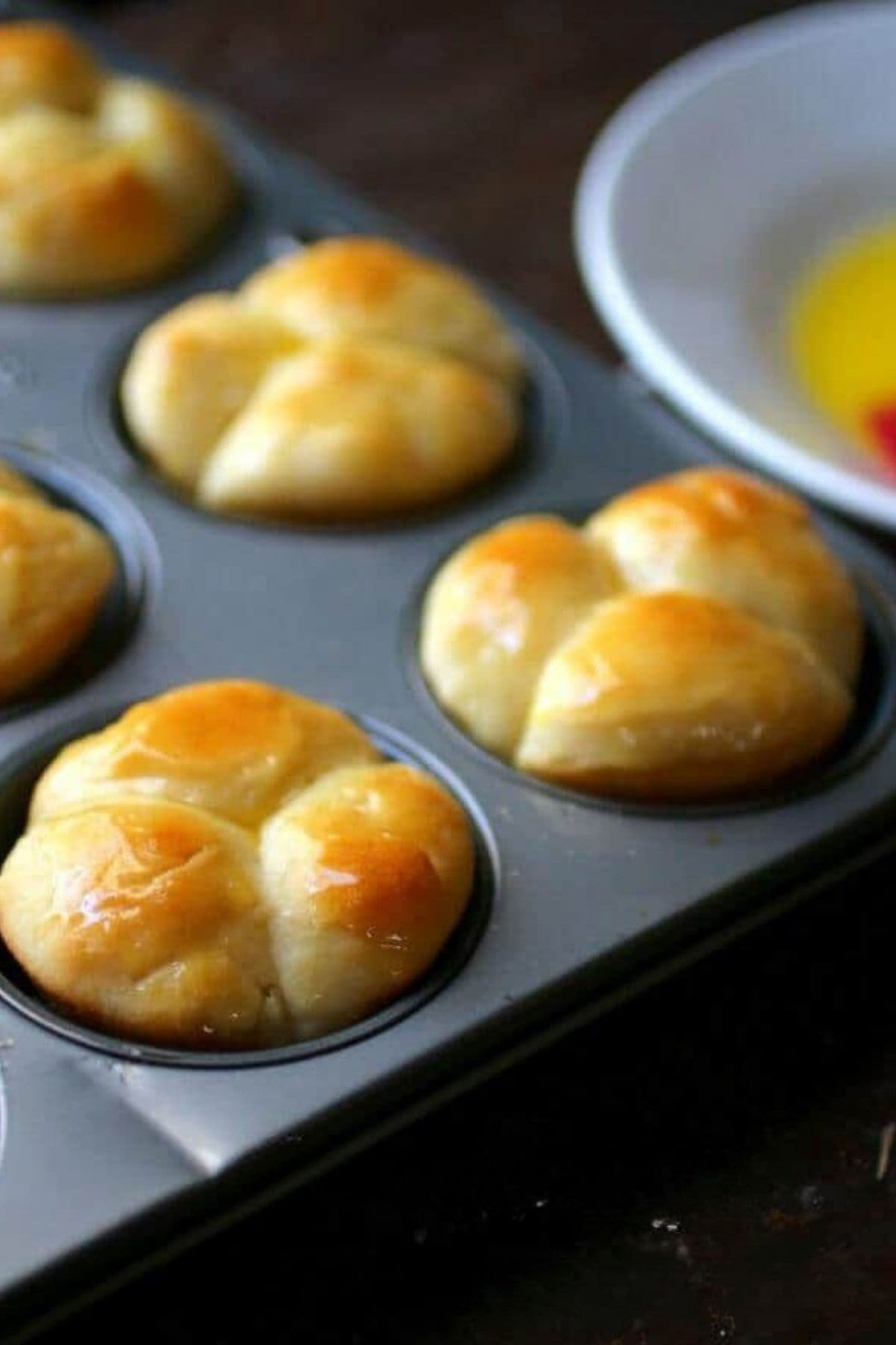 Golden brown cloverleaf dinner rolls in a muffin pan.