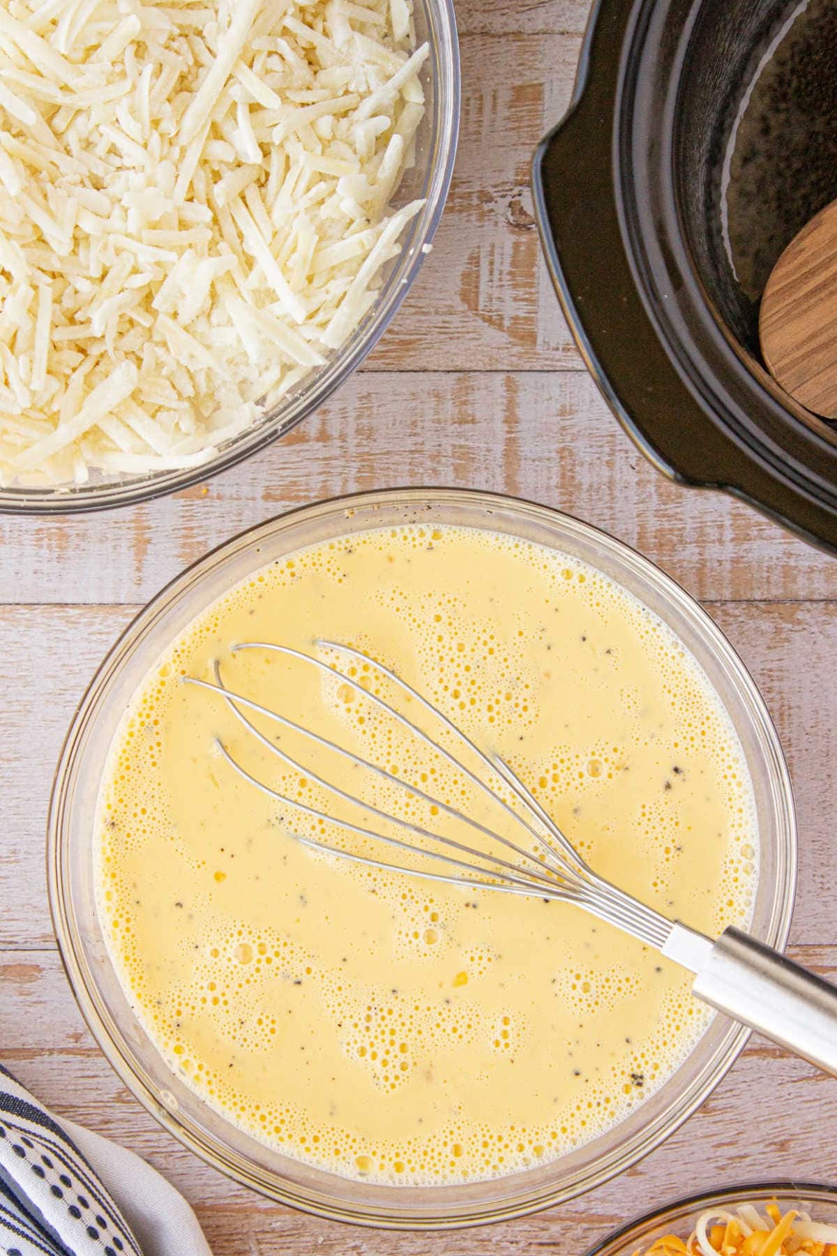 A whisk in a bowl with beaten eggs.