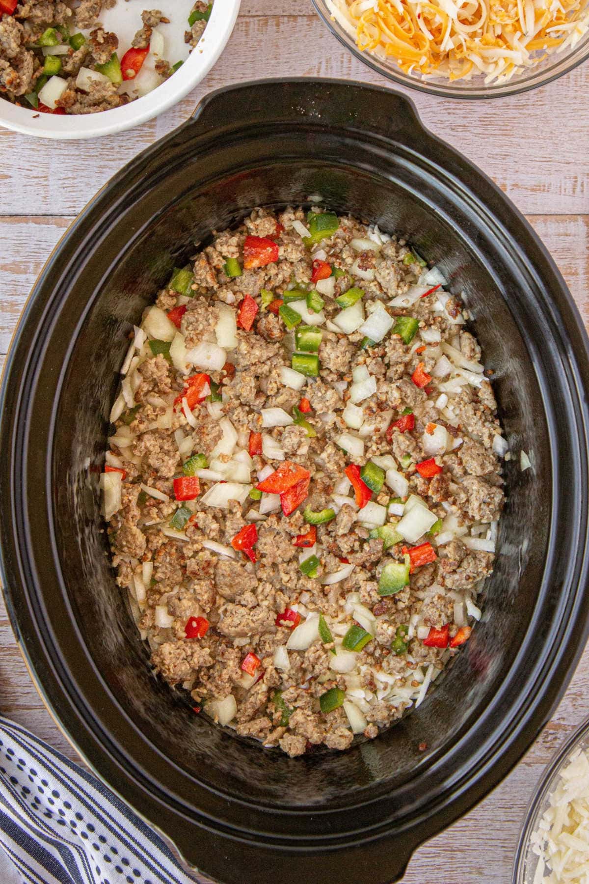 The cooked sausage, onions, and peppers are layered over the cheese in the crockpot.