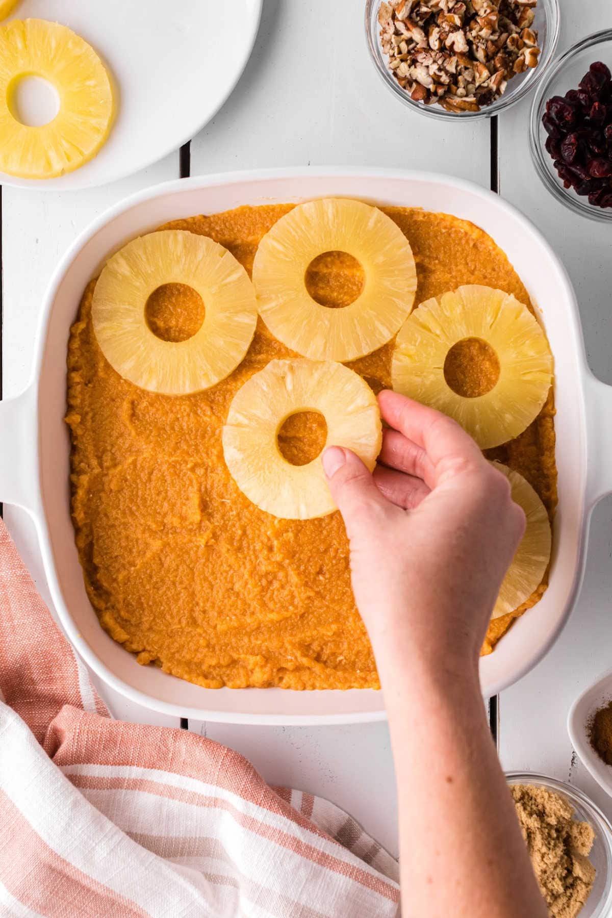 Pineapple rings being placed on whipped sweet potatoes in a casserole.