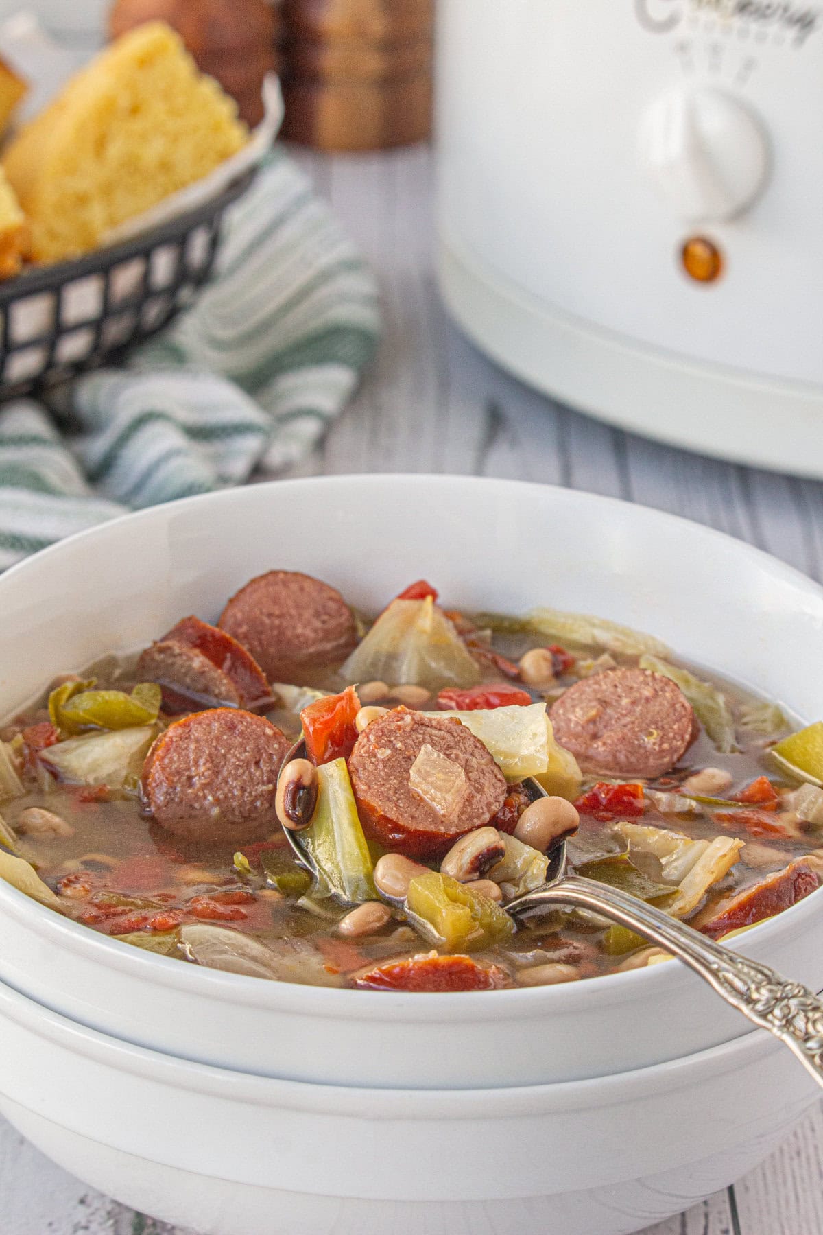 A side-angle view of sausage, black eyed pea, and cabbage soup in a dinner bowl.