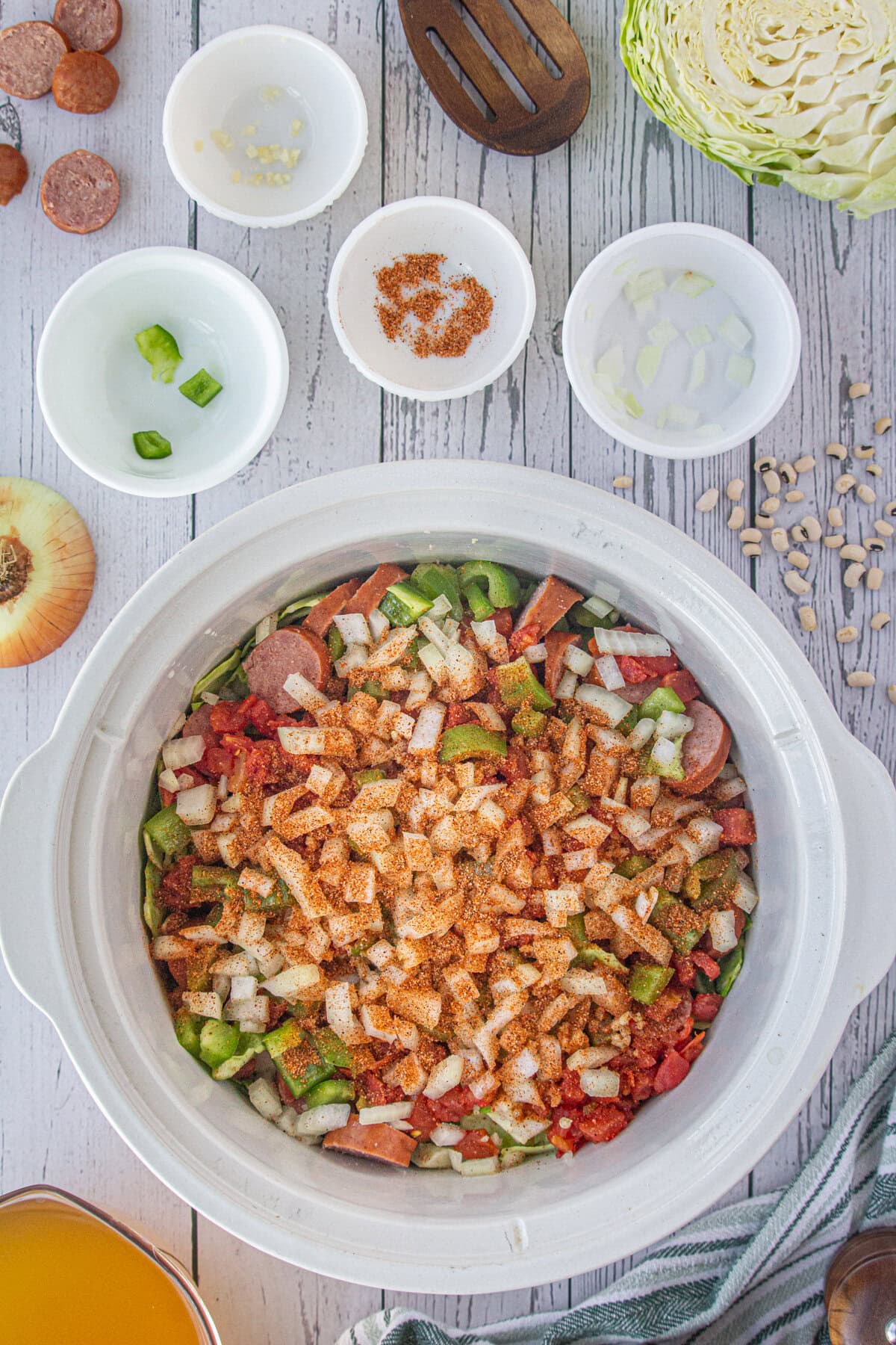 The onions, peppers, and seasonings added to the slow cooker.