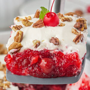 A serving of cherry jello salad with pecans and whipped cream.