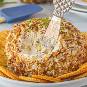 Pineapple cheese ball covered in pecans with a serving knife.