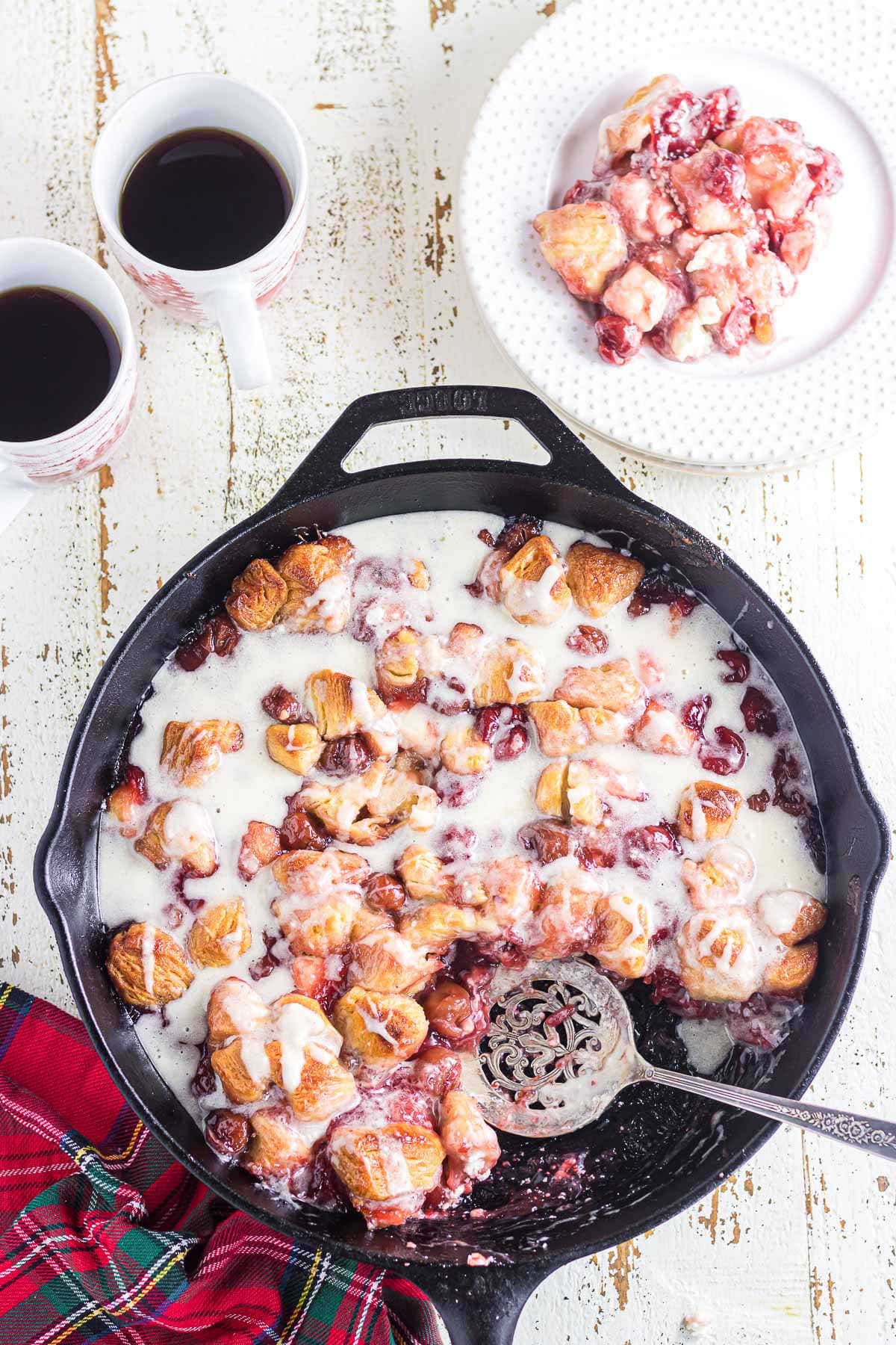 Scooping cherry cream cheese bubble up from a skillet to a serving plate.