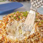 Closeup of the pineapple cheeseball, covered in pecans, with a serving knife in it and a title text overlay for Pinterest.