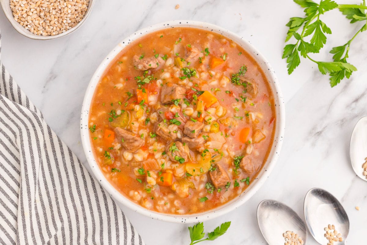 Overhead view of beef and barley soup in a white bowl.