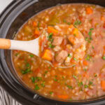 Overhead view of a ladleful of beef and barley soup being removed from the crockpot.