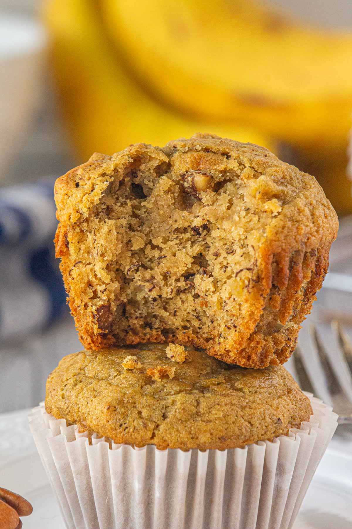 A brown butter banana pecan muffin with a bite taken out stacked on top of another.