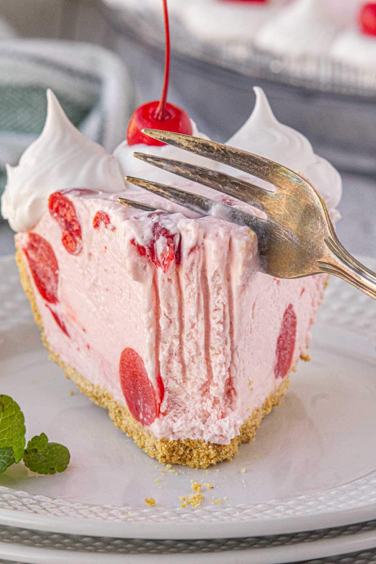 A close-up view of a fork slicing into a piece of cherry icebox pie.