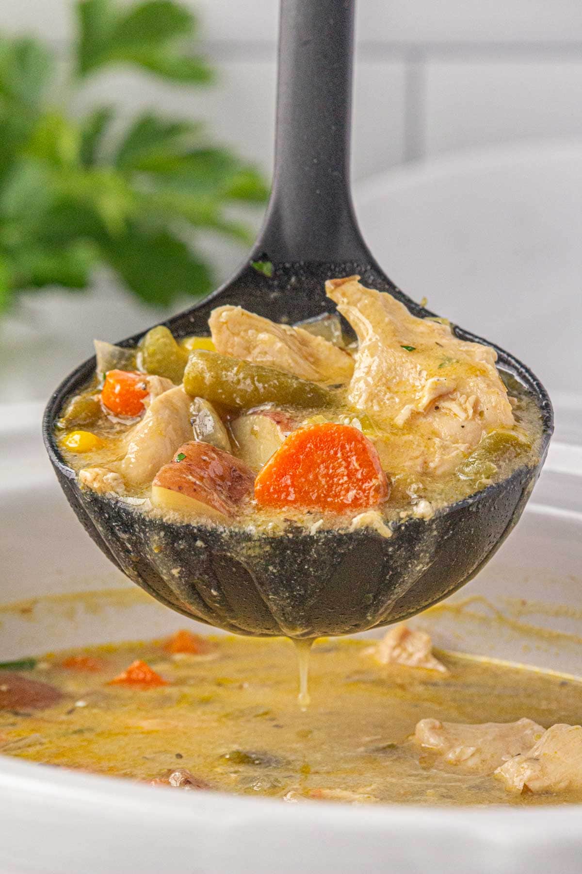 An up-close view of a ladle scooping chicken pot pie soup out of the crockpot.