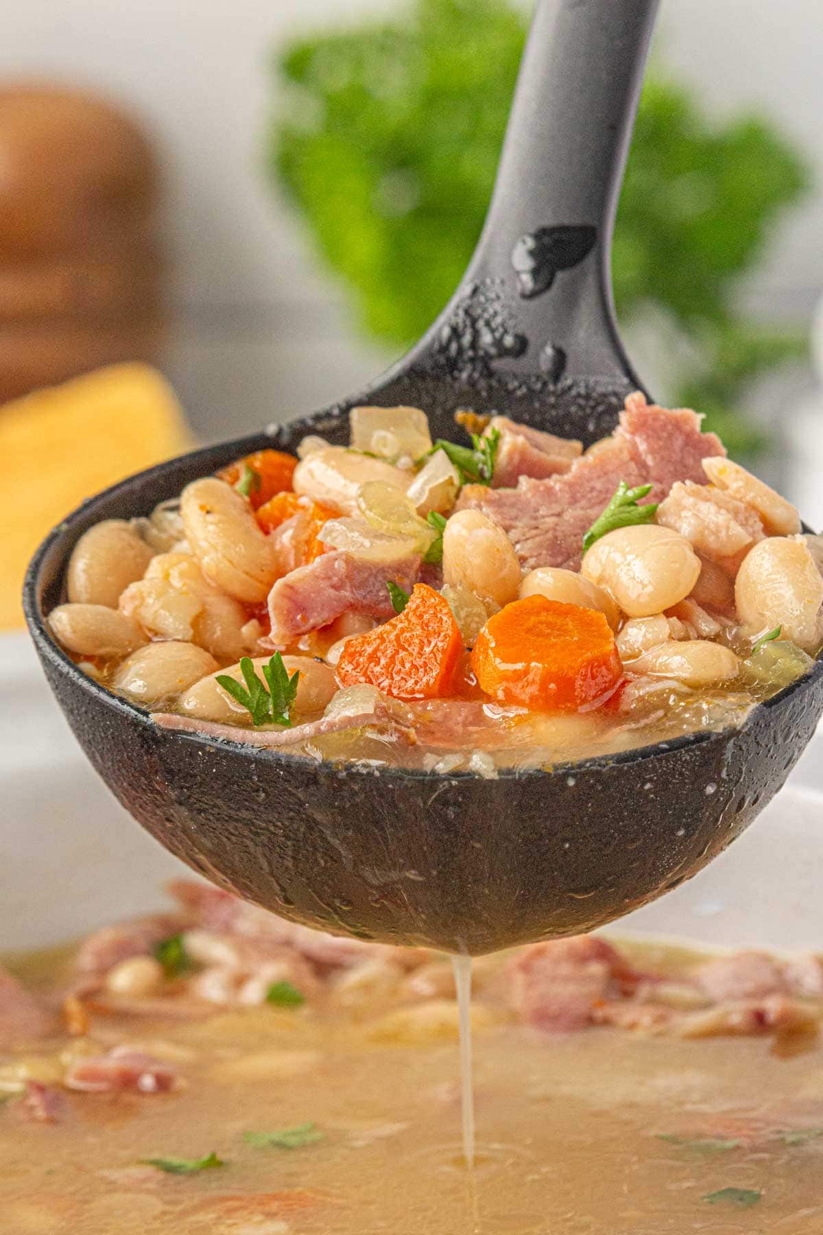 An angled, close-up view of a ladle full of slow cooker ham and bean soup.