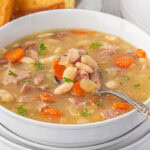 A bowl of ham and bean soup with a spoon in it.