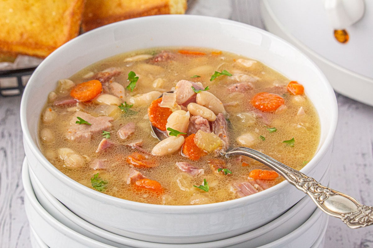 A bowl of ham and bean soup with a spoon in it.