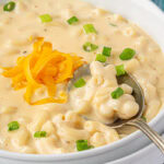 Closeup of macaroni and cheese soup in a white bowl with a spoon.