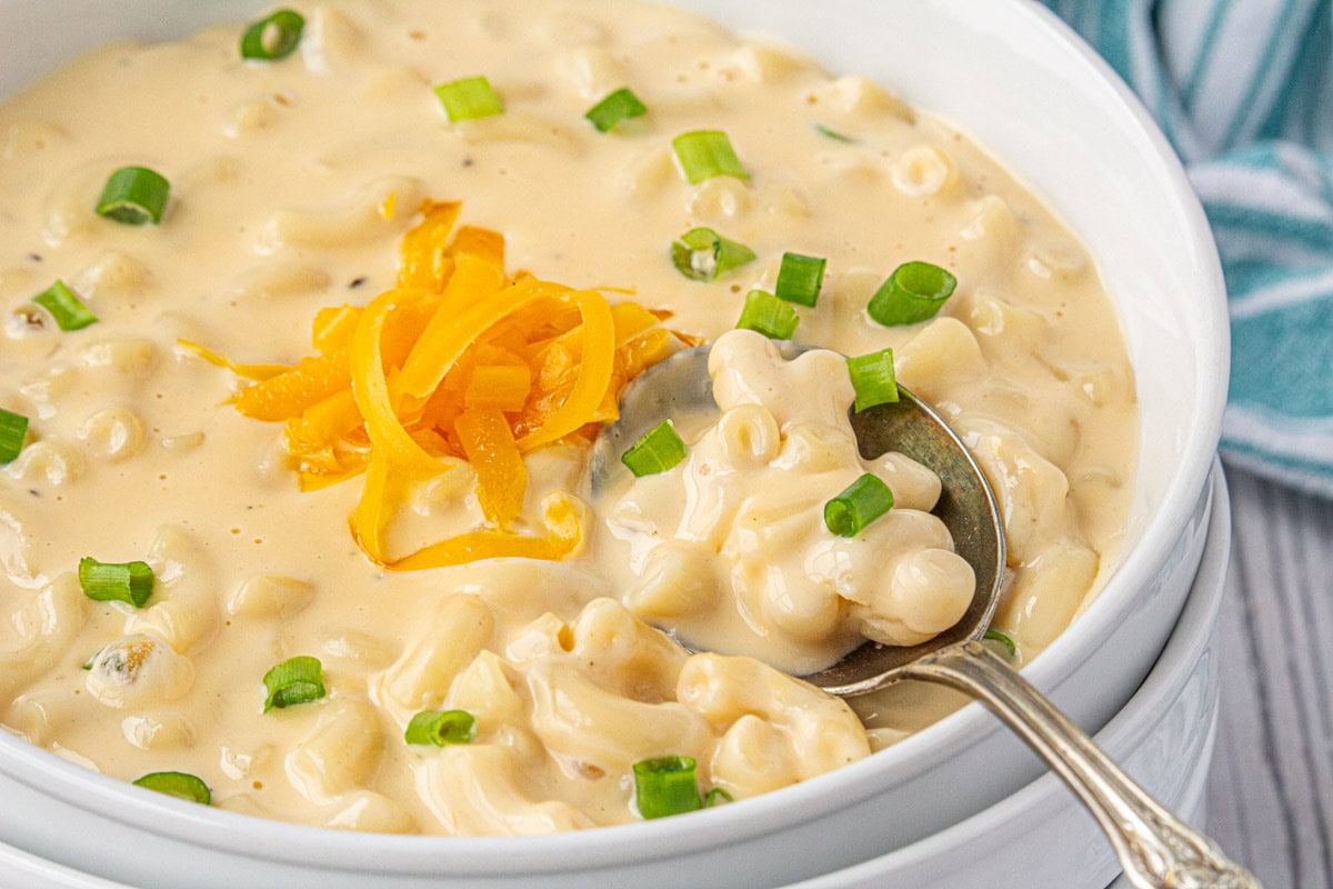 Closeup of macaroni and cheese soup in a white bowl with a spoon.