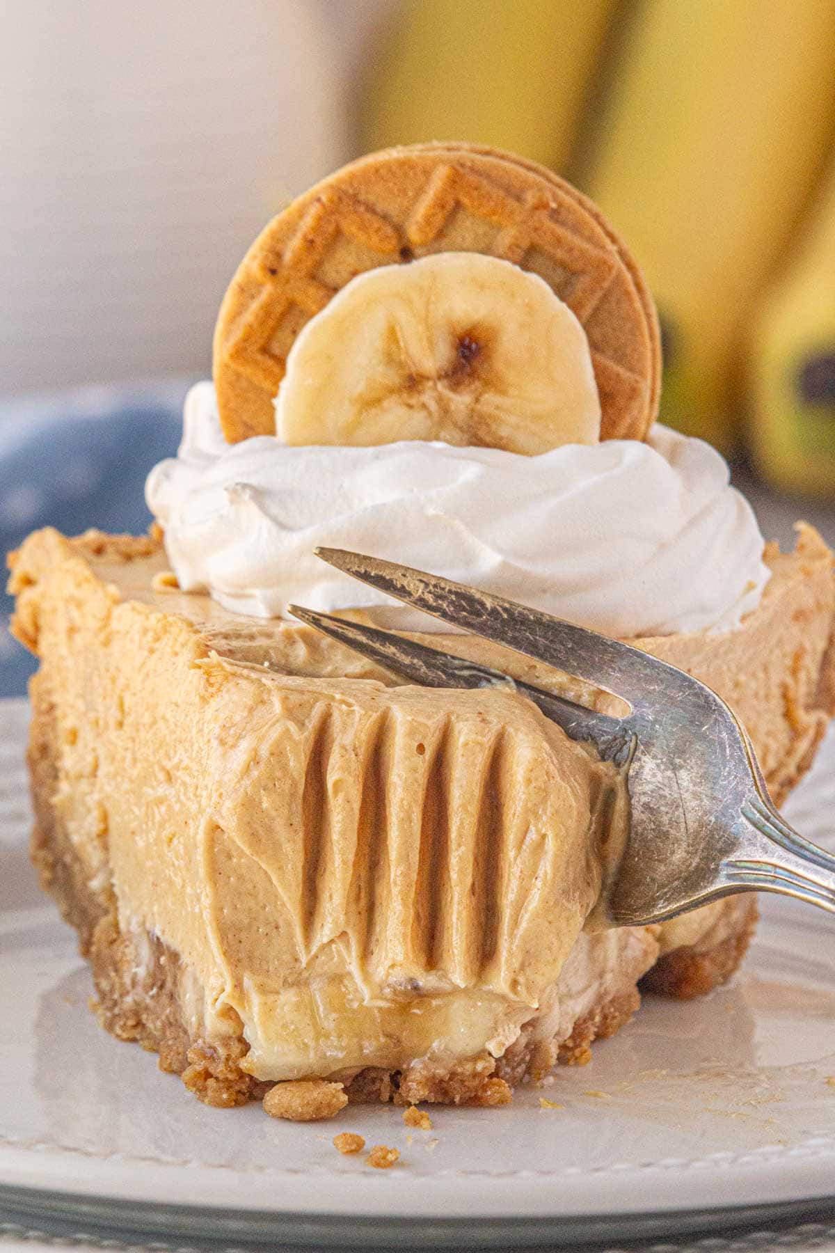 A close-up view of a fork slicing into a piece of peanut butter banana icebox pie.