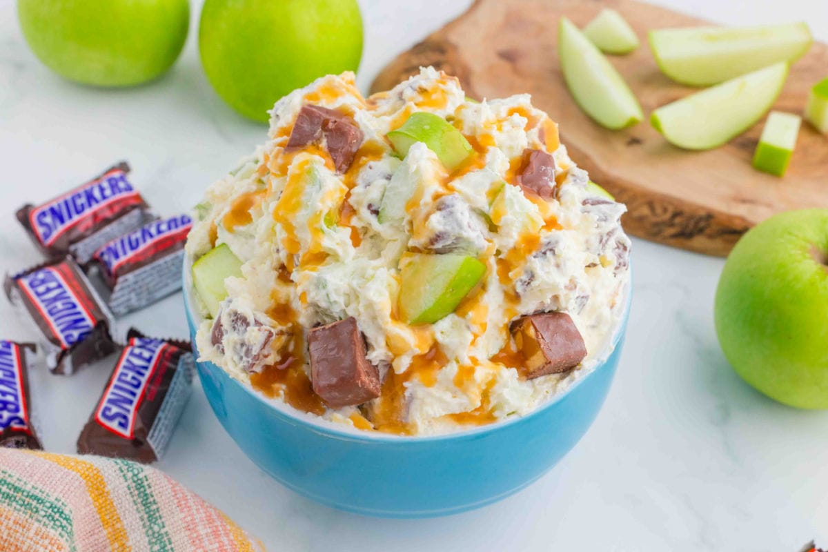 Mixed Snickers bars, green apples, and Cool Whip in a blue bowl.