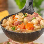 A ladle full of ham and bean soup with a title text overlay for Pinterest.