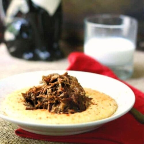 A bowl of cheese grits with pot roast scooped on top.