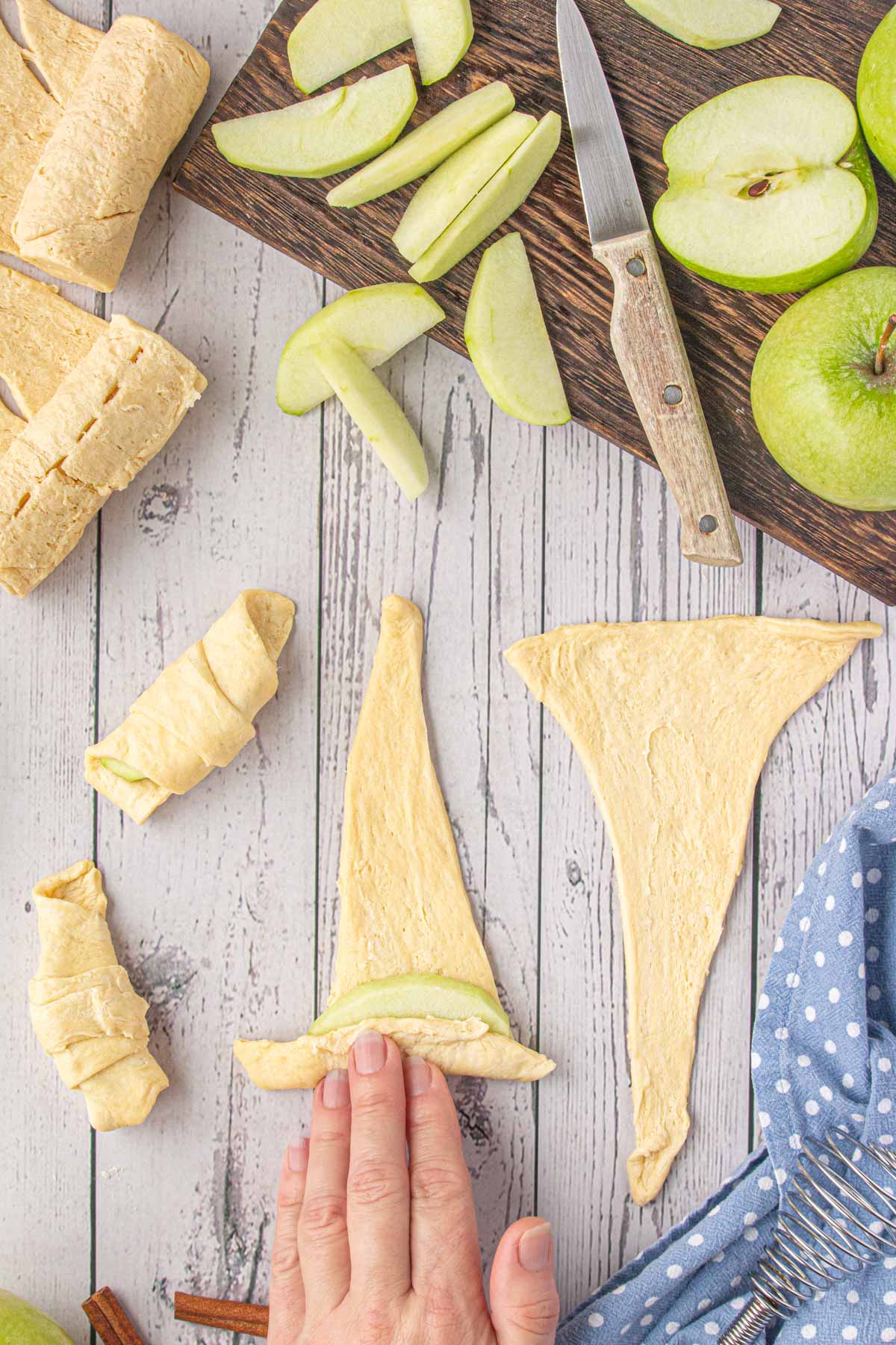 Rolling an apple slice in a piece of crescent roll dough.