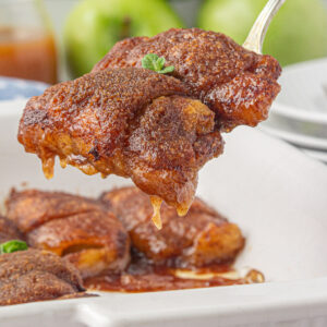 Apple dumplings being served from the pan with caramel sauce dripping down off the serving spoon.