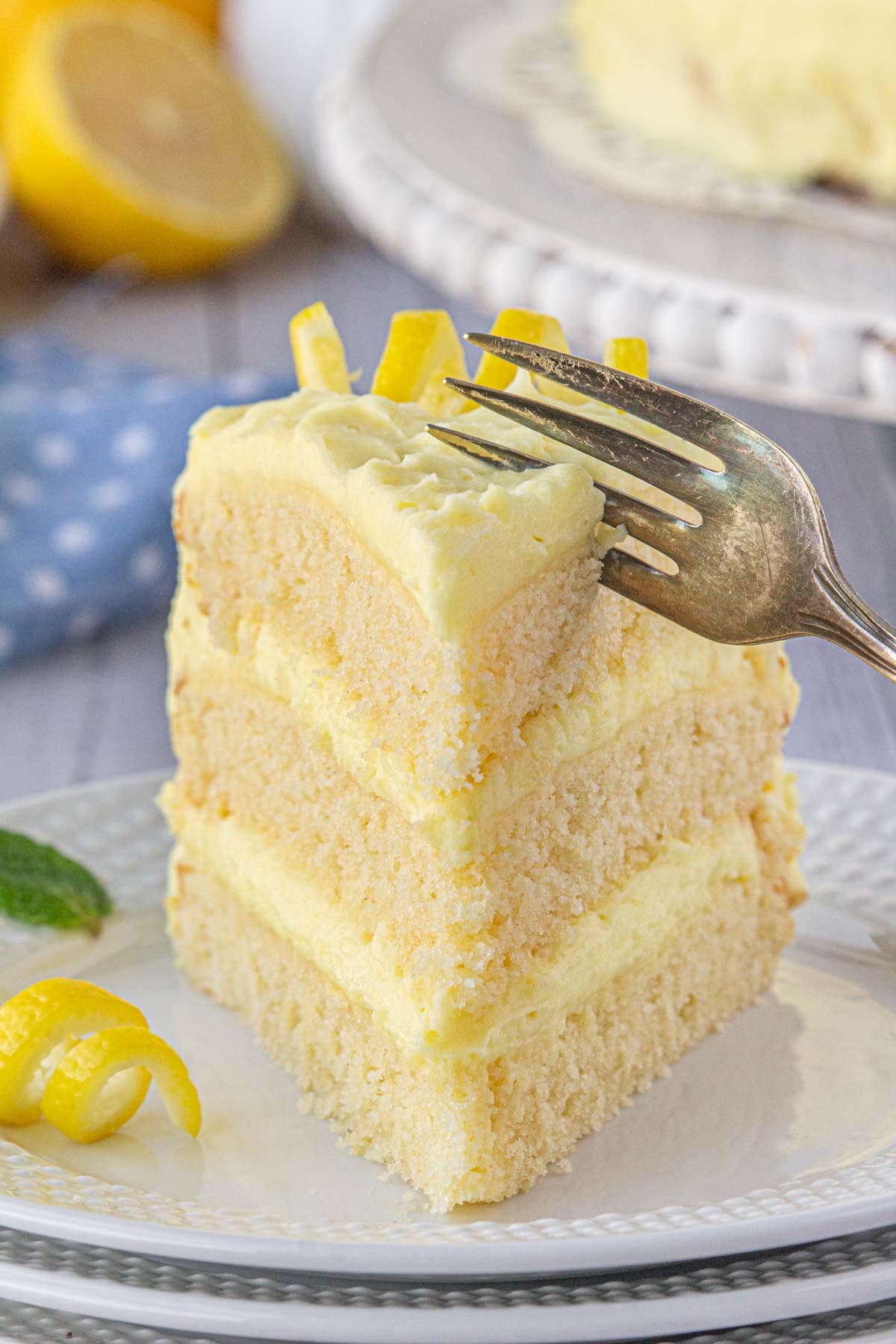 A close-up view of a fork cutting into a slice of moist lemon cake.