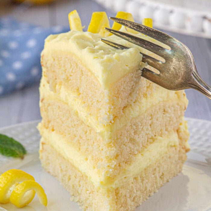 A slice of lemon layer cake with a fork cutting into it.