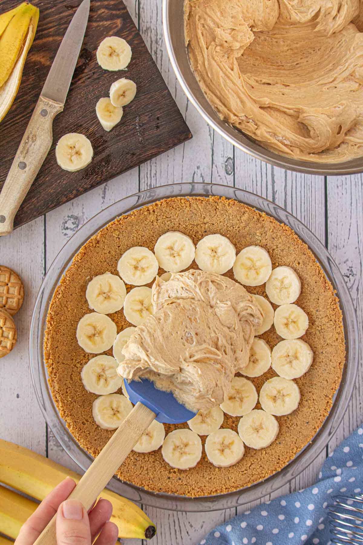 Spreading the peanut butter filling over banana slices in the pie crust.