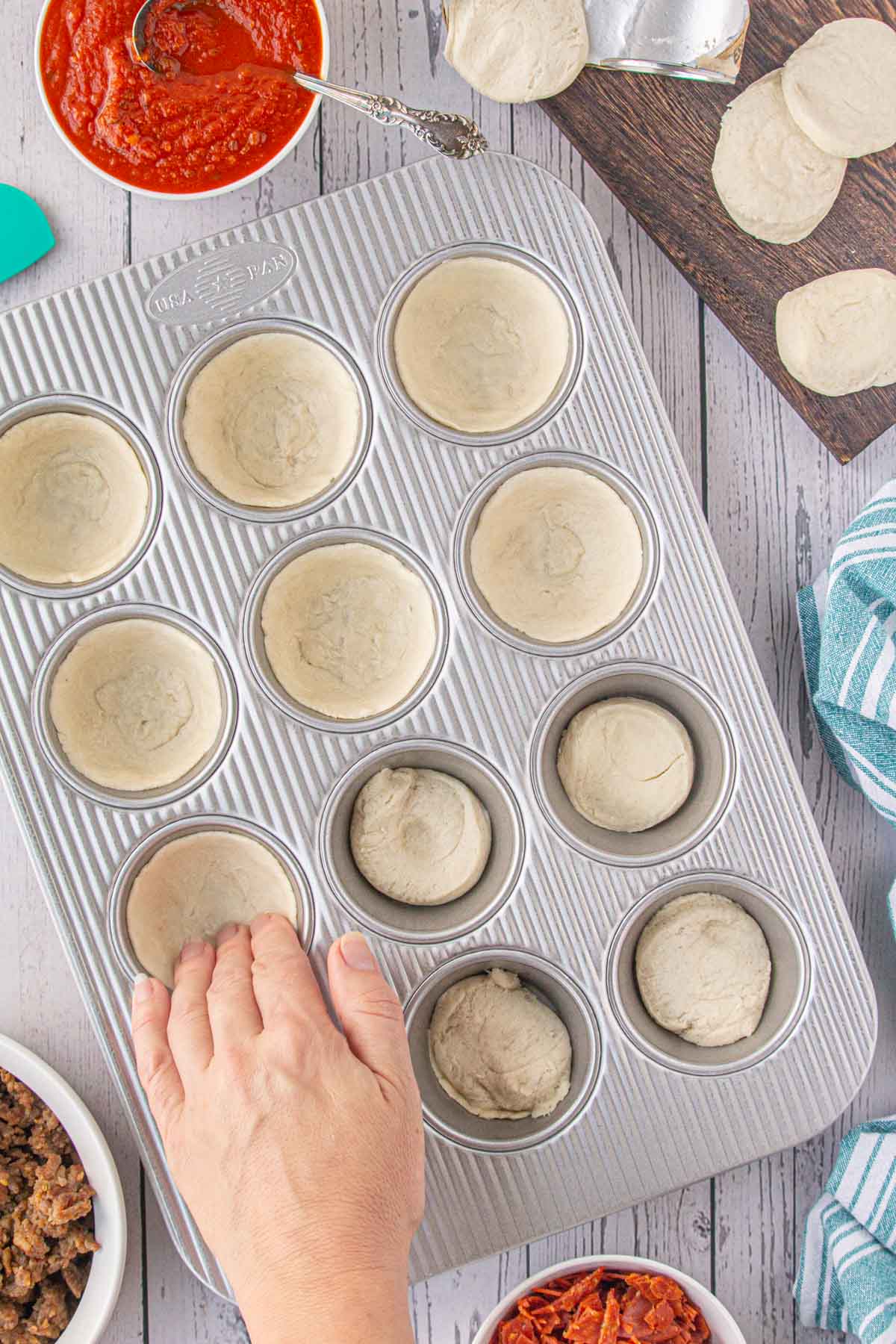 Pressing the biscuit dough into the wells of a muffin tin. 