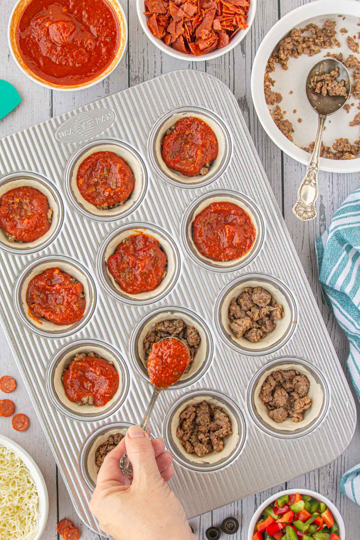 Spooning pizza sauce over the ground beef in the pizza cups.