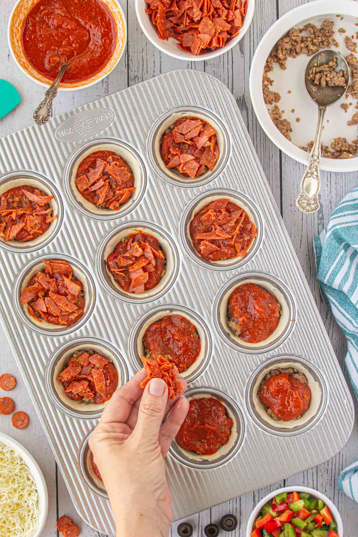 Sprinkling pepperoni over the pizza cups.