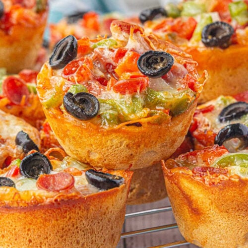 Closeup of pizza cups filled with ground beef, pepperoni, olives, pizza sauce, and cheese.