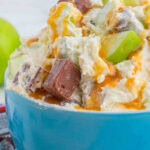 Closeup of a blue bowl with chopped green apples and chopped chocolate bars in a creamy dressing. Title text overlay for Pinterest.